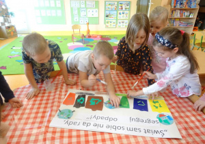 Czwórka dzieci dekoruje plakat ekologiczny, naklejają elementy z kolorowego papieru.